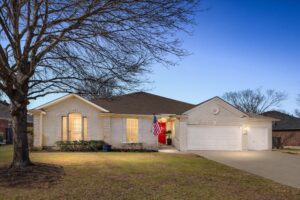 Front exterior of the Round Rock Assisted Living home at dusk with a mature shade tree and two-car garage