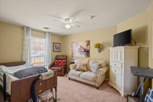 Private resident bedroom with a care bed, dresser, television, and comfortable seating
